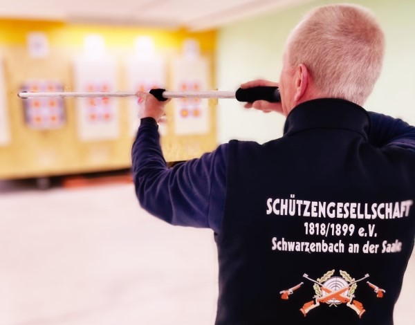 Mann mit Blasrohr auf Scheibe zielend